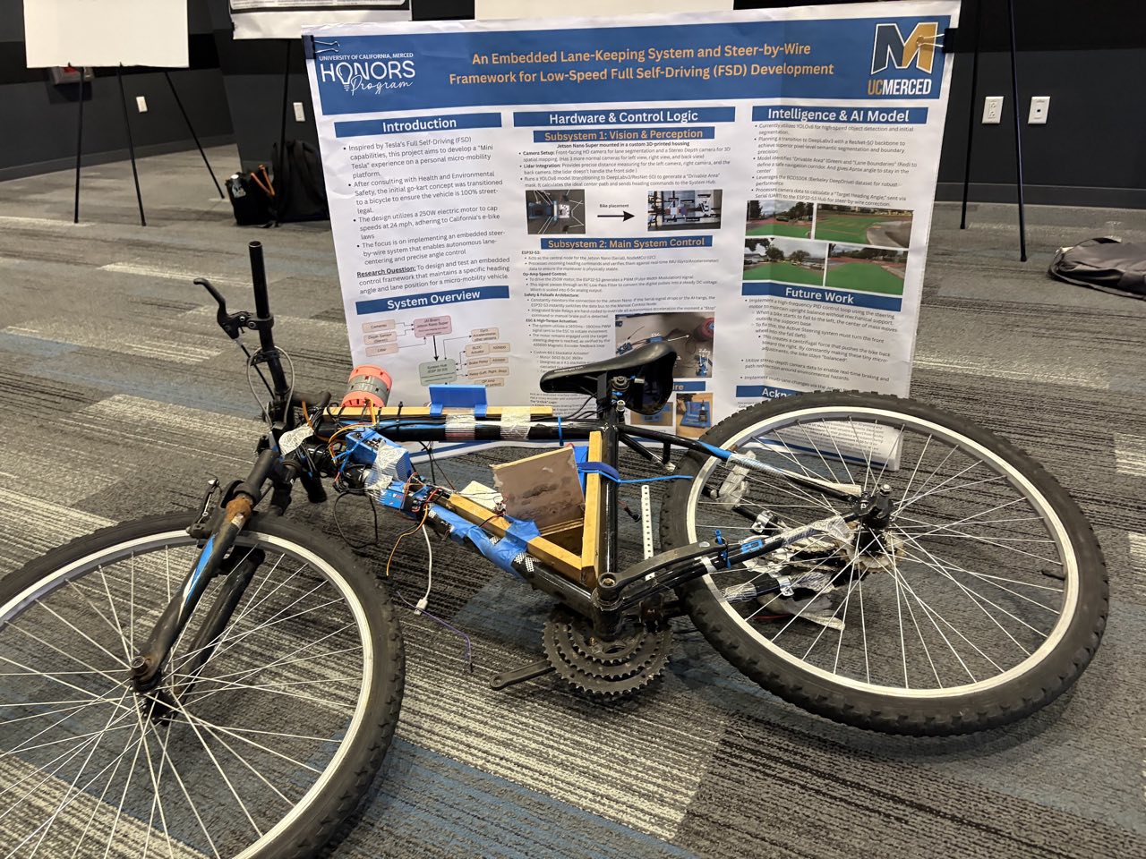 Autonomous bicycle prototype with exposed perception and control hardware displayed in front of its research poster